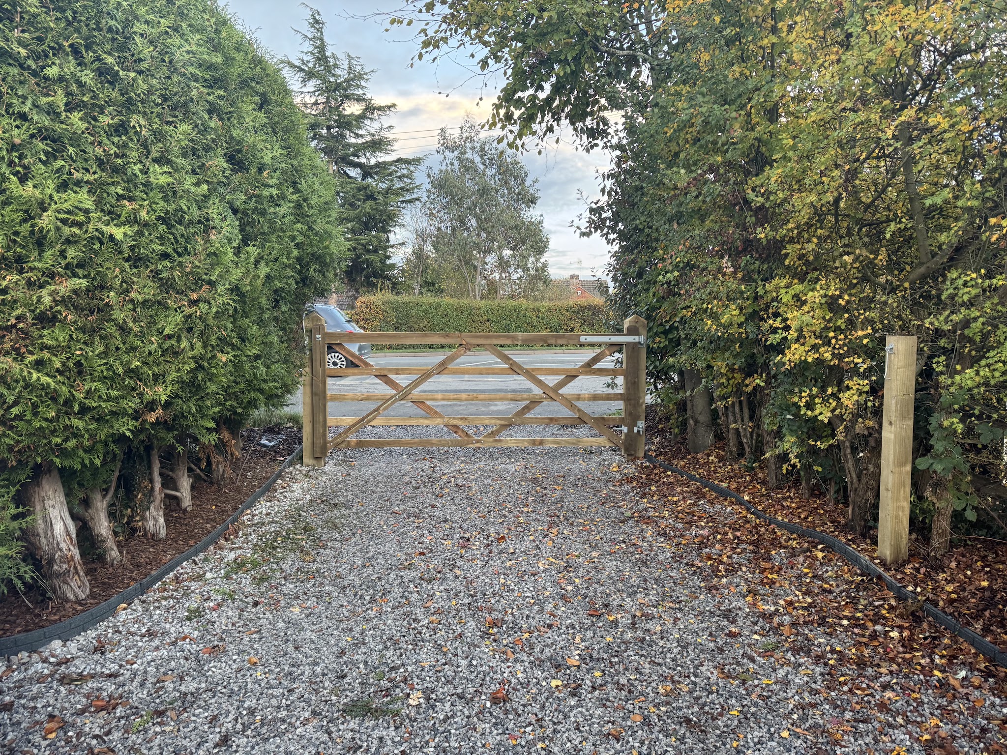 A five-bar wooden gate across a gravel drive between hedges